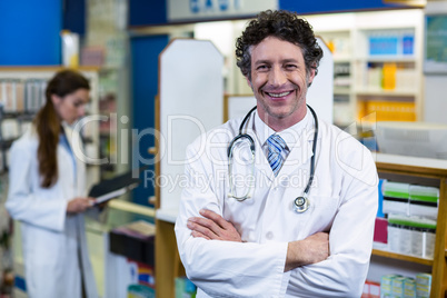 Pharmacist standing with arms crossed in pharmacy