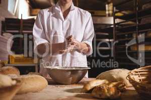 Mid-section of female baker spreading flour in a bowl