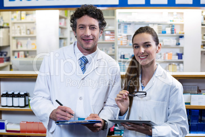 Smiling pharmacists with clipboard and digital tablet in pharmac