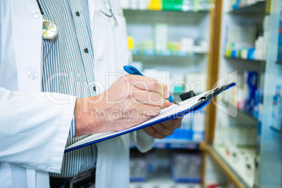 Pharmacist writing on clipboard in pharmacy