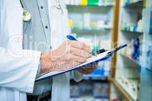 Pharmacist writing on clipboard in pharmacy