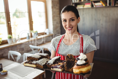 Portrait of female baker holding a tray of sweet foods