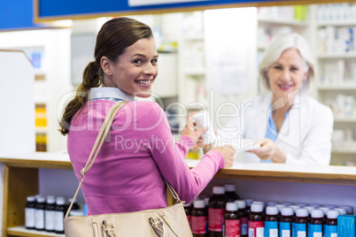 Smiling customer and pharmacist holding medicine in pharmacy