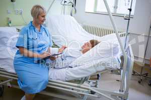 Nurse writing on clipboard while interacting with a patient