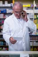 Pharmacist talking on mobile phone while checking prescription