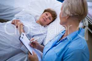 Patient lying on bed while nurse writing on clipboard