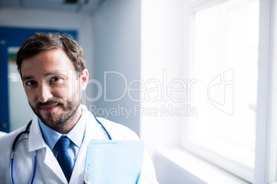 Confident doctor with clipboard standing in hospital corridor