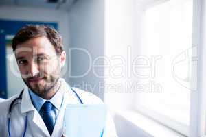 Confident doctor with clipboard standing in hospital corridor