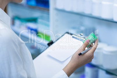 Pharmacist writing on clipboard while checking medicine