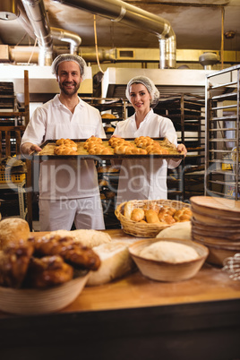 Portrait of female and male baker holding a tray of michetta