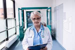 Confident female doctor with clipboard standing in hospital corr