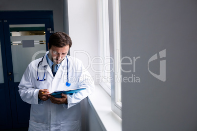 Doctor standing in corridor looking at clipboard Doctor standing in corridor looking at clipboard