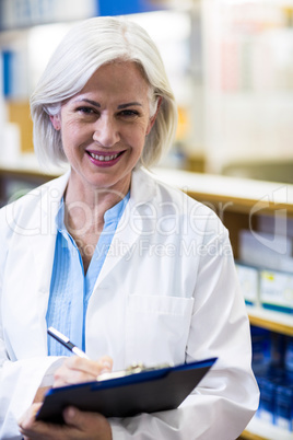 Pharmacist writing on clipboard in pharmacy