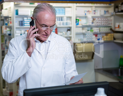 Pharmacist talking on mobile phone while checking prescription