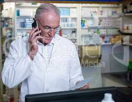 Pharmacist talking on mobile phone while checking prescription