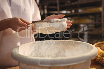 Mid-section of female baker sifting flour through a sieve