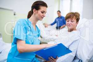 Nurse showing clipboard to patient in hospital ward