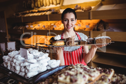 Portrait of female baker holding a tray of sweet foods