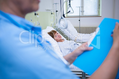 Nurse holding file while senior patient lying on bed in backgrou