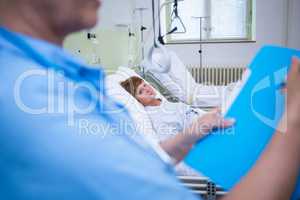 Nurse holding file while senior patient lying on bed in backgrou