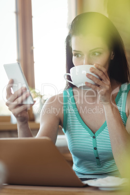 Woman using mobile phone while having coffee