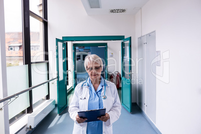 Doctor standing in corridor looking at clipboard