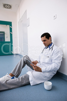 Doctor sitting on floor and using digital tablet in corridor