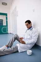 Doctor sitting on floor and using digital tablet in corridor