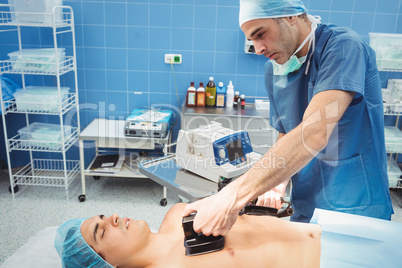 Male surgeon resuscitating an unconscious patient with a defibri