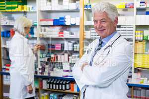 Pharmacist standing with arms crossed and co-worker checking med