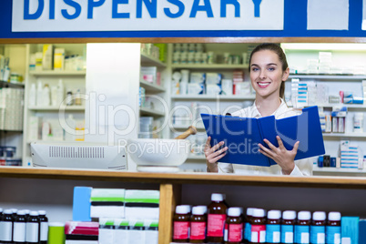 Pharmacist looking in clipboard at counter in pharmacy