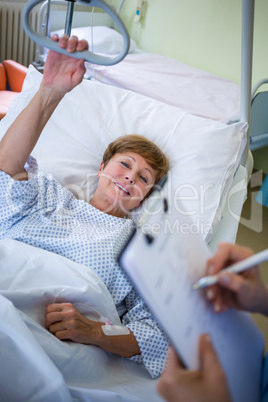 Patient lying on bed while nurse writing on clipboard