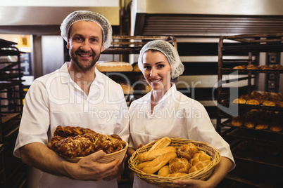 Portrait of female and male baker holding basket of bread and sw
