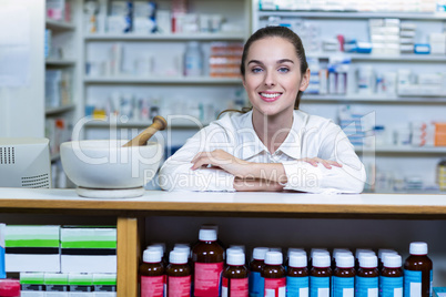 Smiling pharmacist sitting at counter in pharmacy