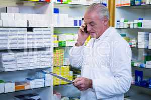 Pharmacist talking on mobile phone while checking medicines
