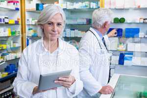 Pharmacist using digital tablet and co-worker checking medicines