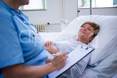 Nurse writing on clipboard while interacting with a patient