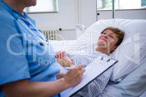 Nurse writing on clipboard while interacting with a patient