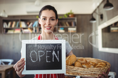 Portrait of female baker holding open signboard