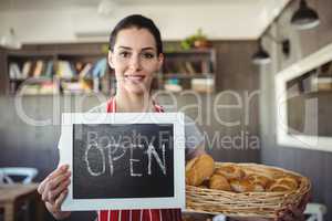 Portrait of female baker holding open signboard