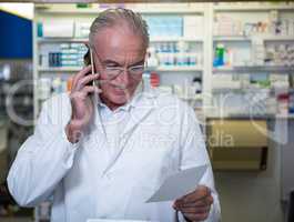 Pharmacist talking on mobile phone while checking prescription