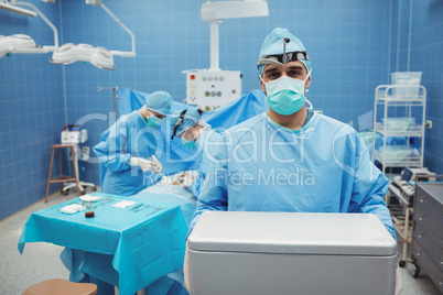 Portrait of surgeon holding ice box while colleagues performing