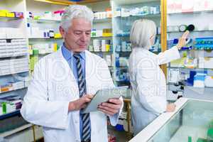 Pharmacist using digital tablet and co-worker checking medicines