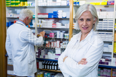 Pharmacist standing with arms crossed and co-worker checking med
