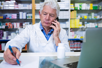 Pharmacist talking on mobile phone while writing prescriptions