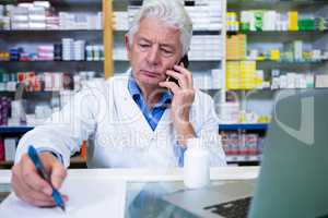 Pharmacist talking on mobile phone while writing prescriptions