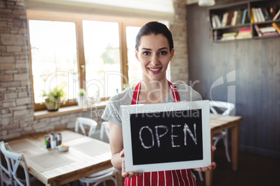 Portrait of female baker holding open signboard