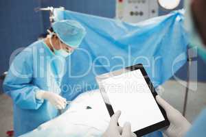 Surgeon using digital while nurse operating patient in operation