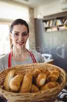 Portrait of female baker holding a basket of bread loafs