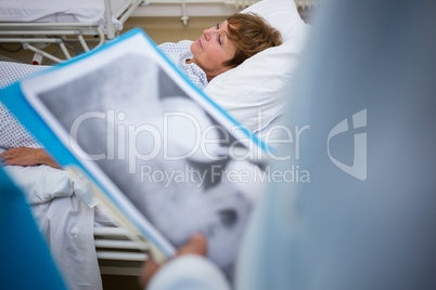 Patient lying on bed while doctor holding medical report